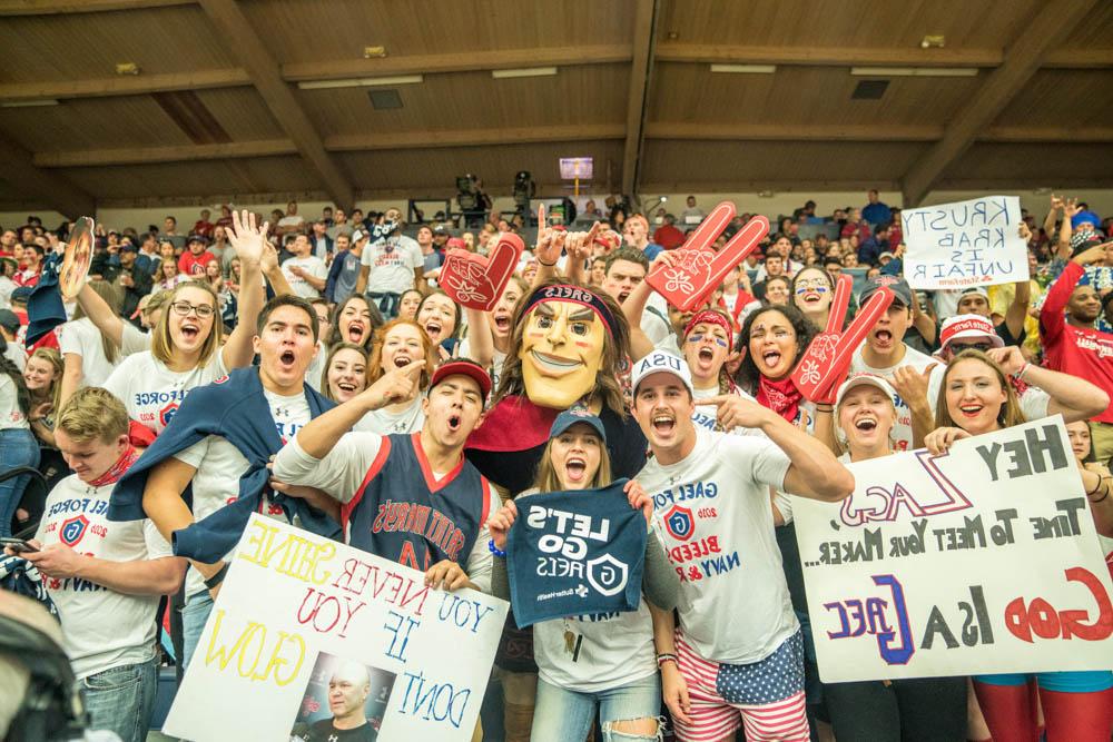 Students cheering and holding signs at a basketball game with Gideon the mascot