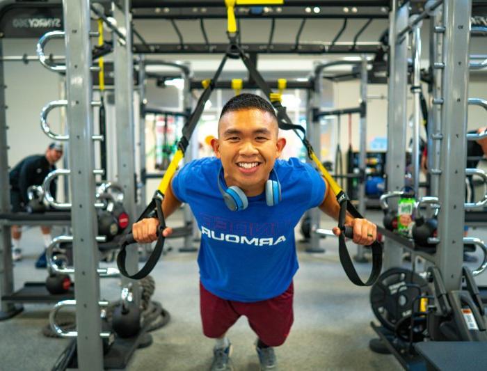 一个学生在健身房里的健身器材上微笑着俯下身